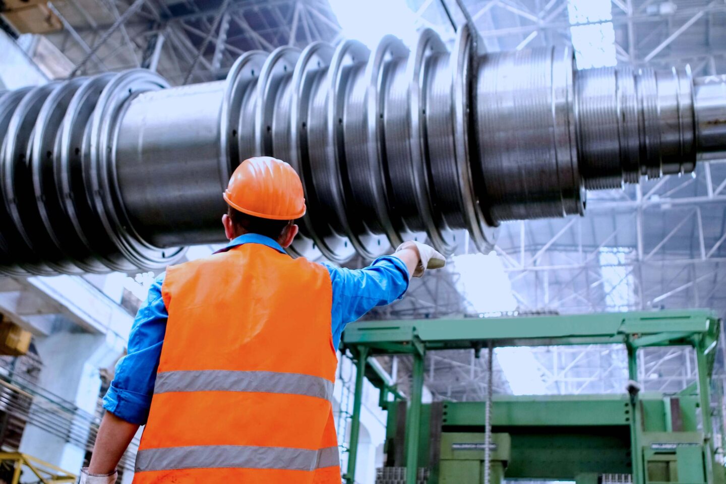 Ein Mann steht in Warnweste und mit Schutzhelm vor einem großen Maschinenbauteil aus Metall.