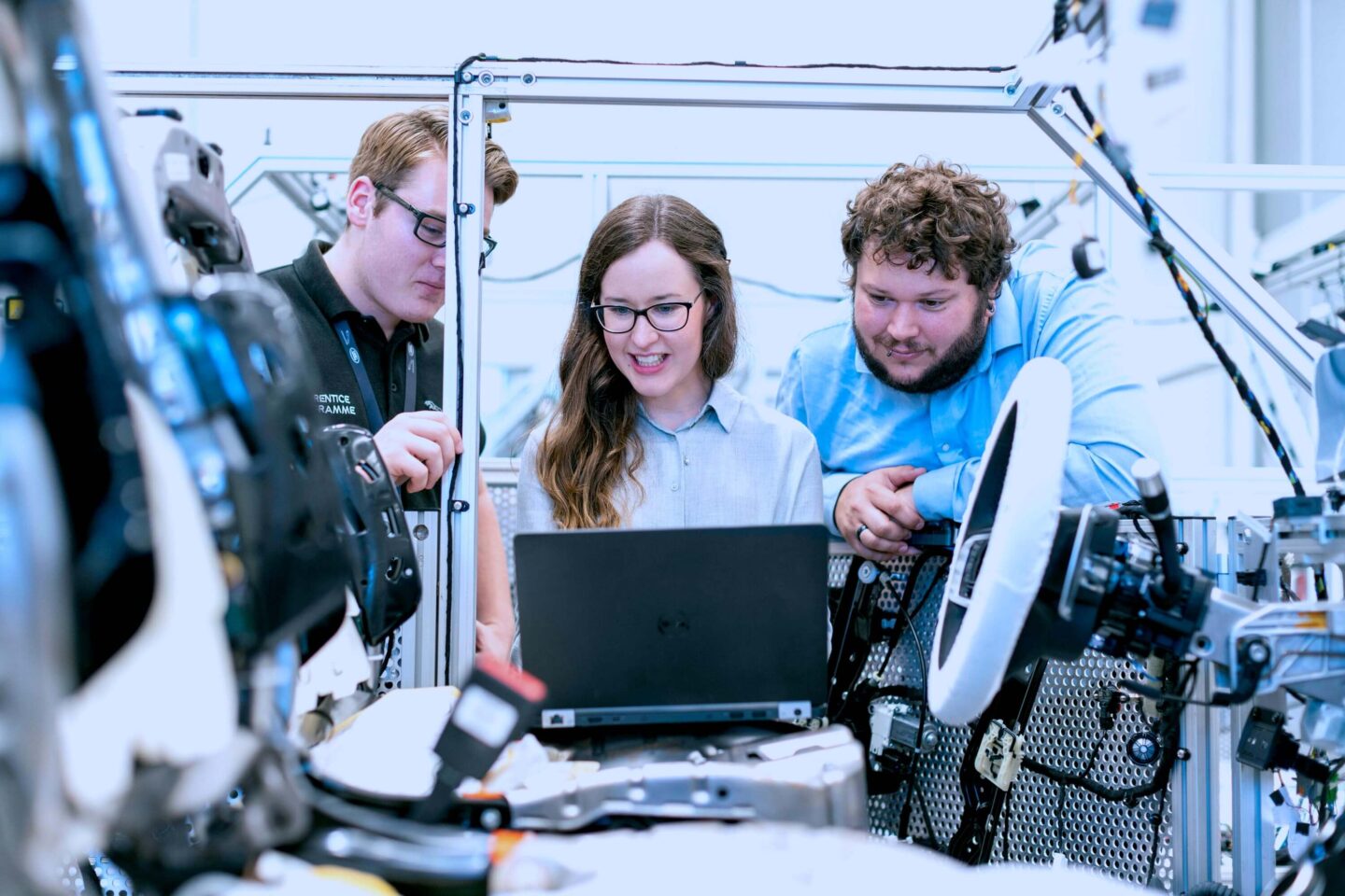 Drei Personen beugen sich über einen Laptop inmitten einer Automobilproduktion